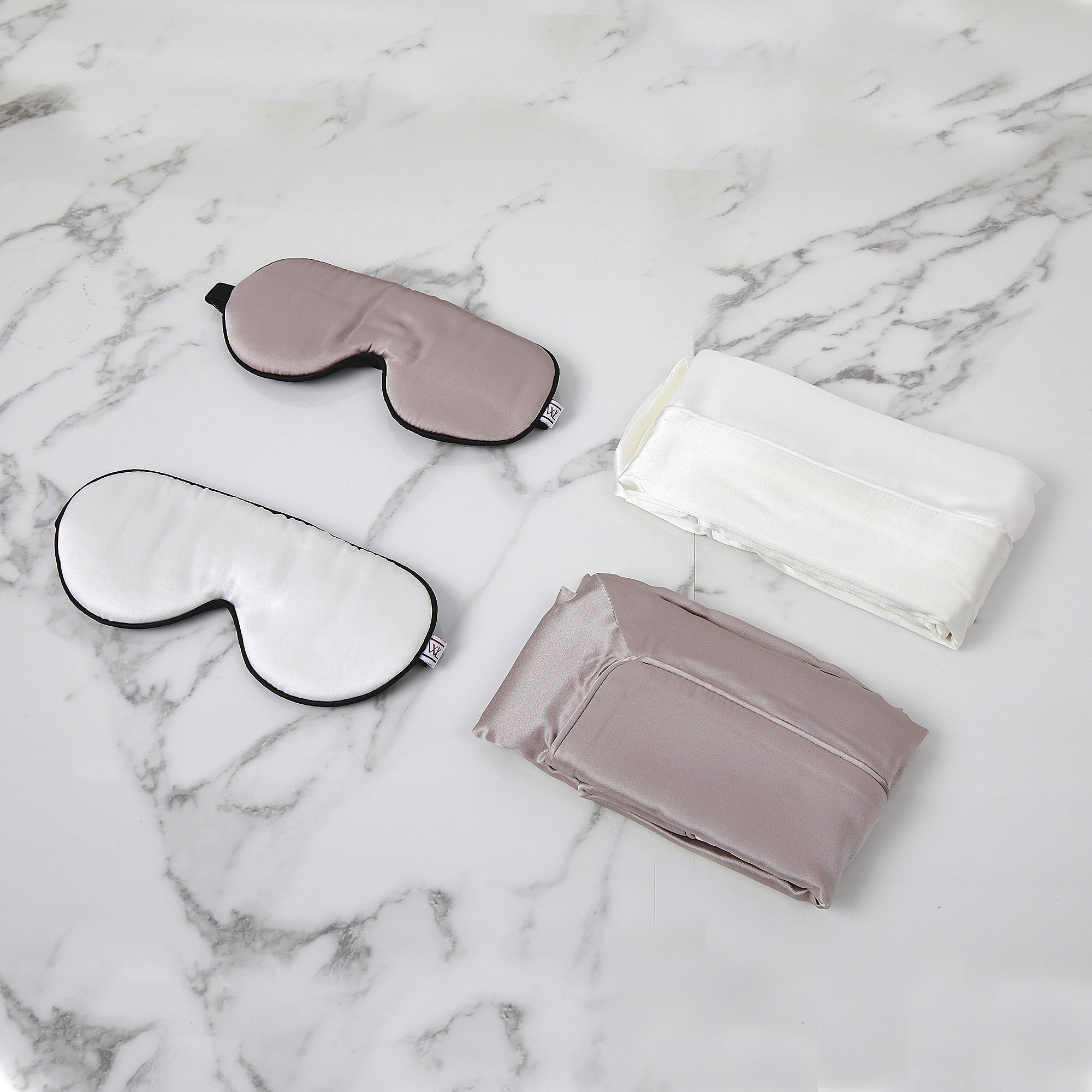 A photo of a pearl grey silk eye mask and pillowcase and a white eye mask and pillowcase