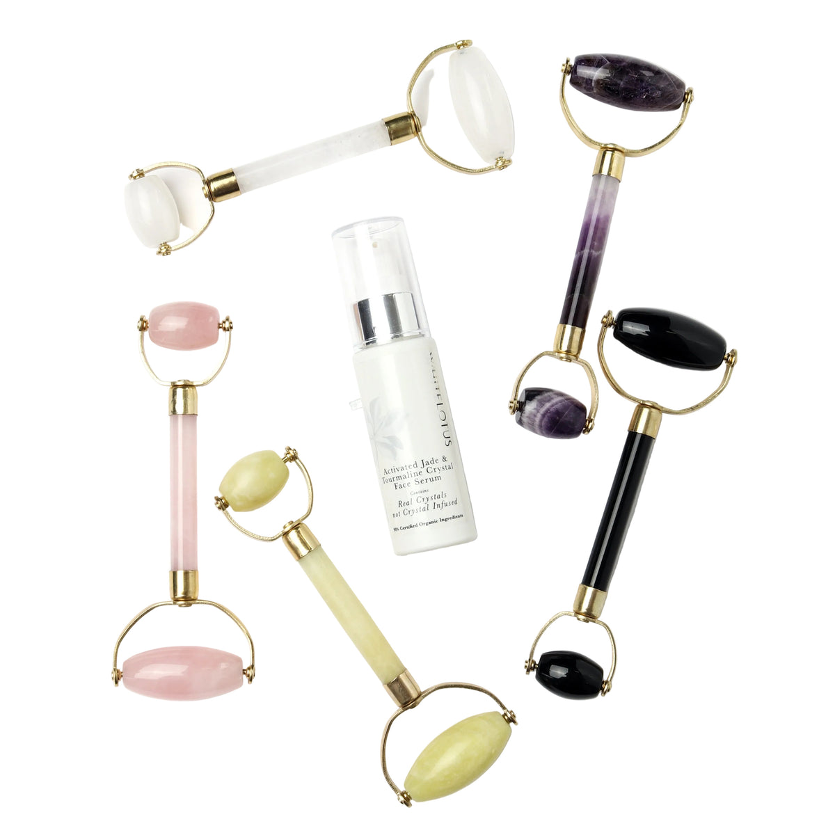 Five jade rollers in different stone colors (pink, purple, black, and white) arranged around a bottle of Gold Skin Cellularity facial serum on a white background.