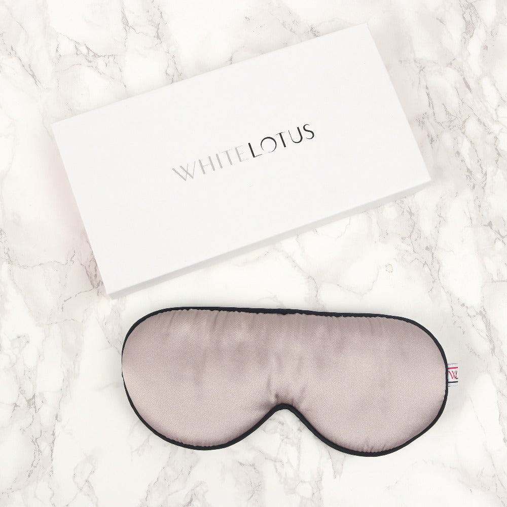 a pearl grey silk eye mask and it's packaging box on a marble background